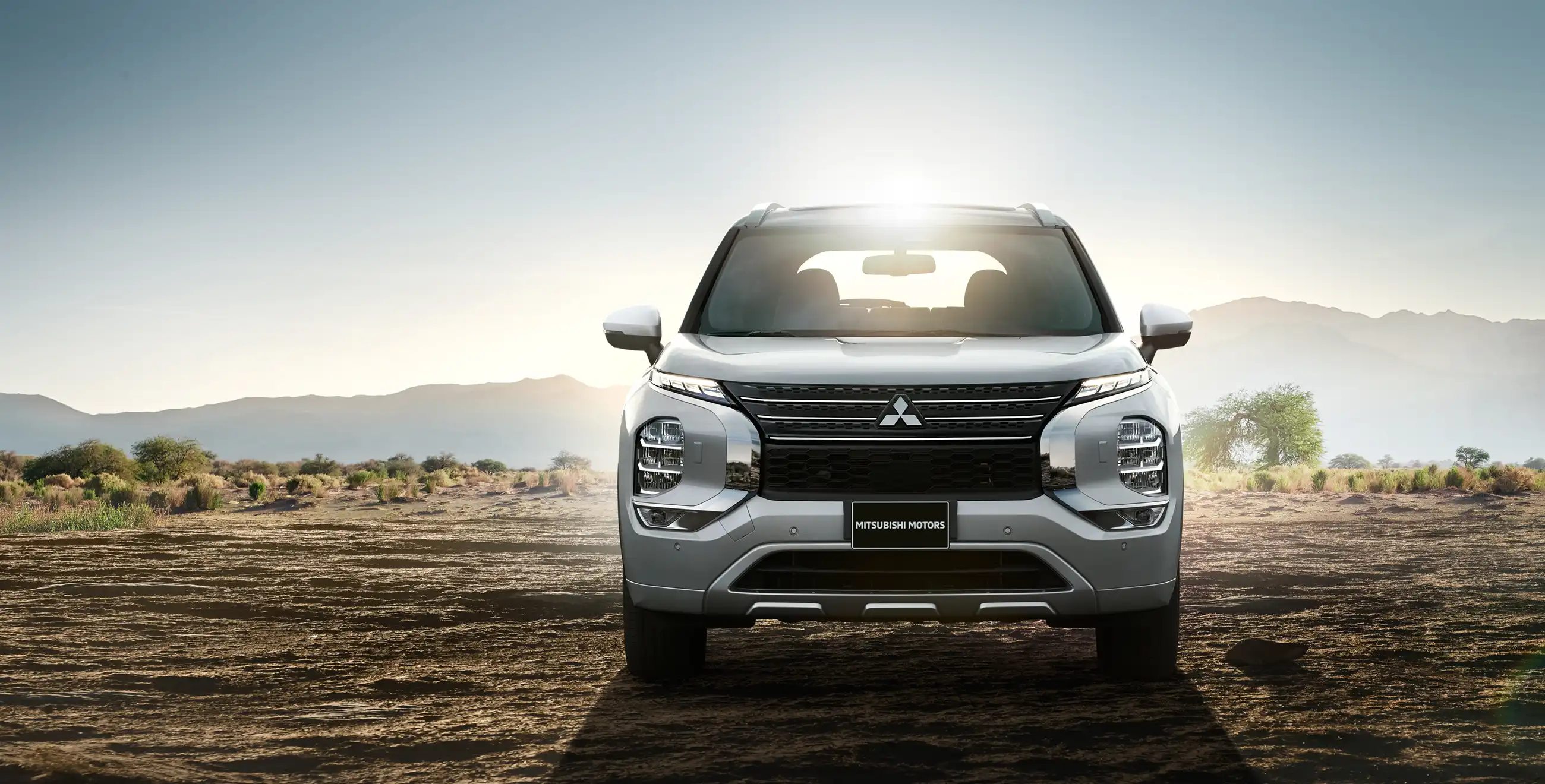 A 2024 Mitsubishi Outlander PHEV SUV in the desert with mountains and the sunset behind