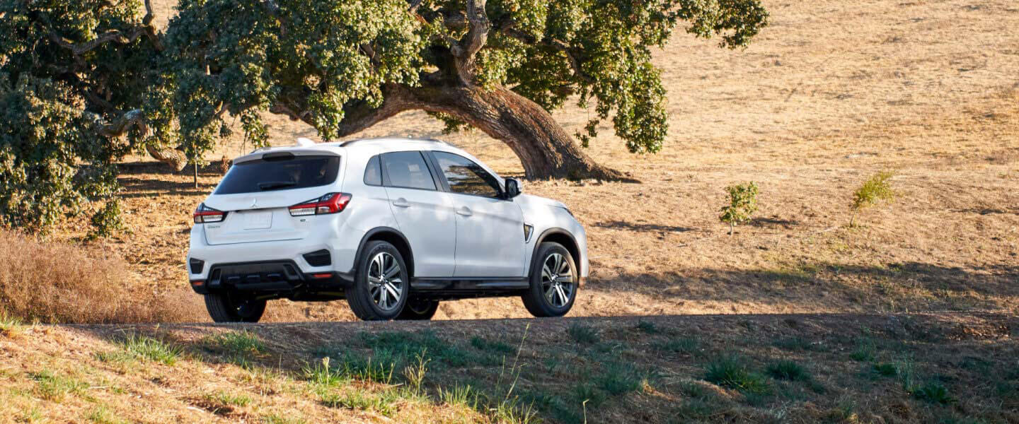 Rear and side view of a white 2024 Mitsubishi RVR driving on a rural road