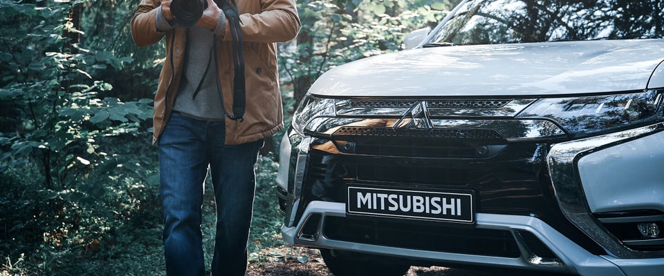 Photographer in the wilderness walking away from his white 2022 Mitsubishi Outlander PHEV electric SUV