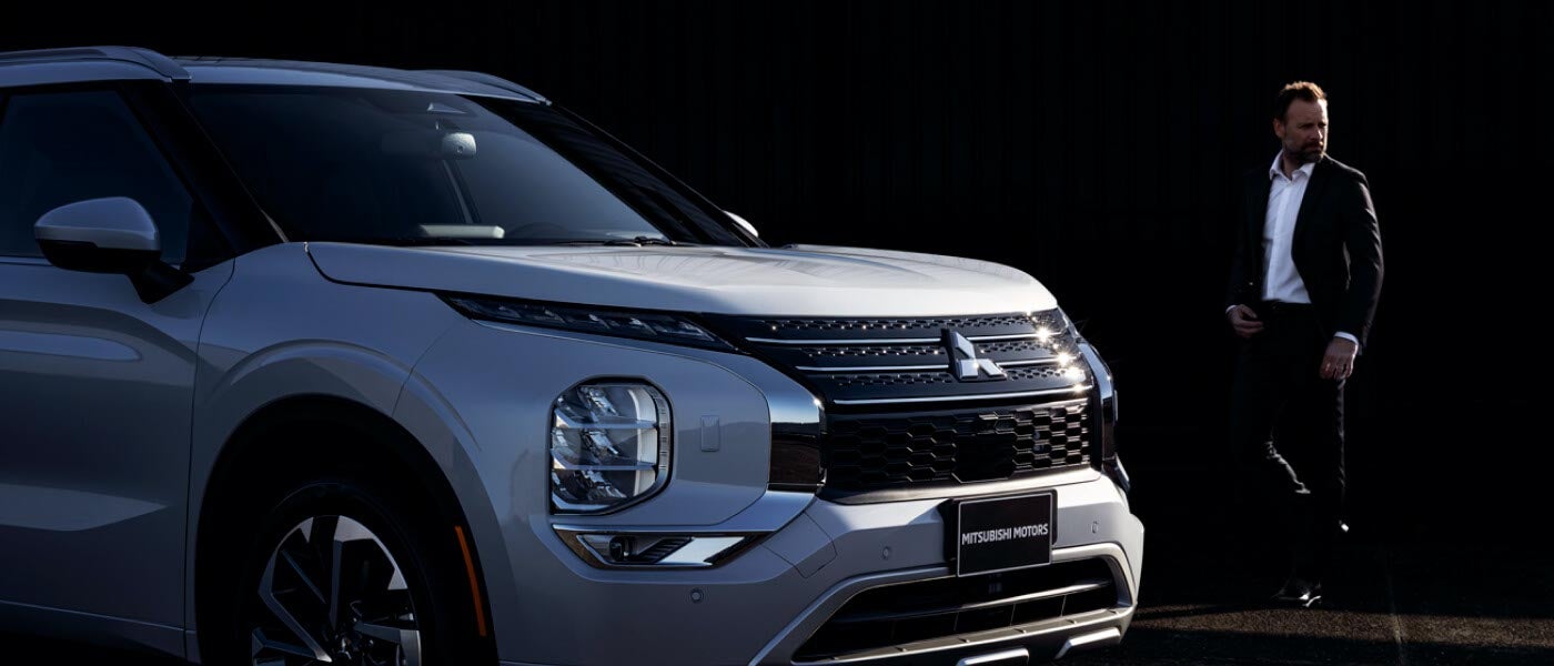 Man walking towards a parked white 2023 Mitsubishi Outlander SUV