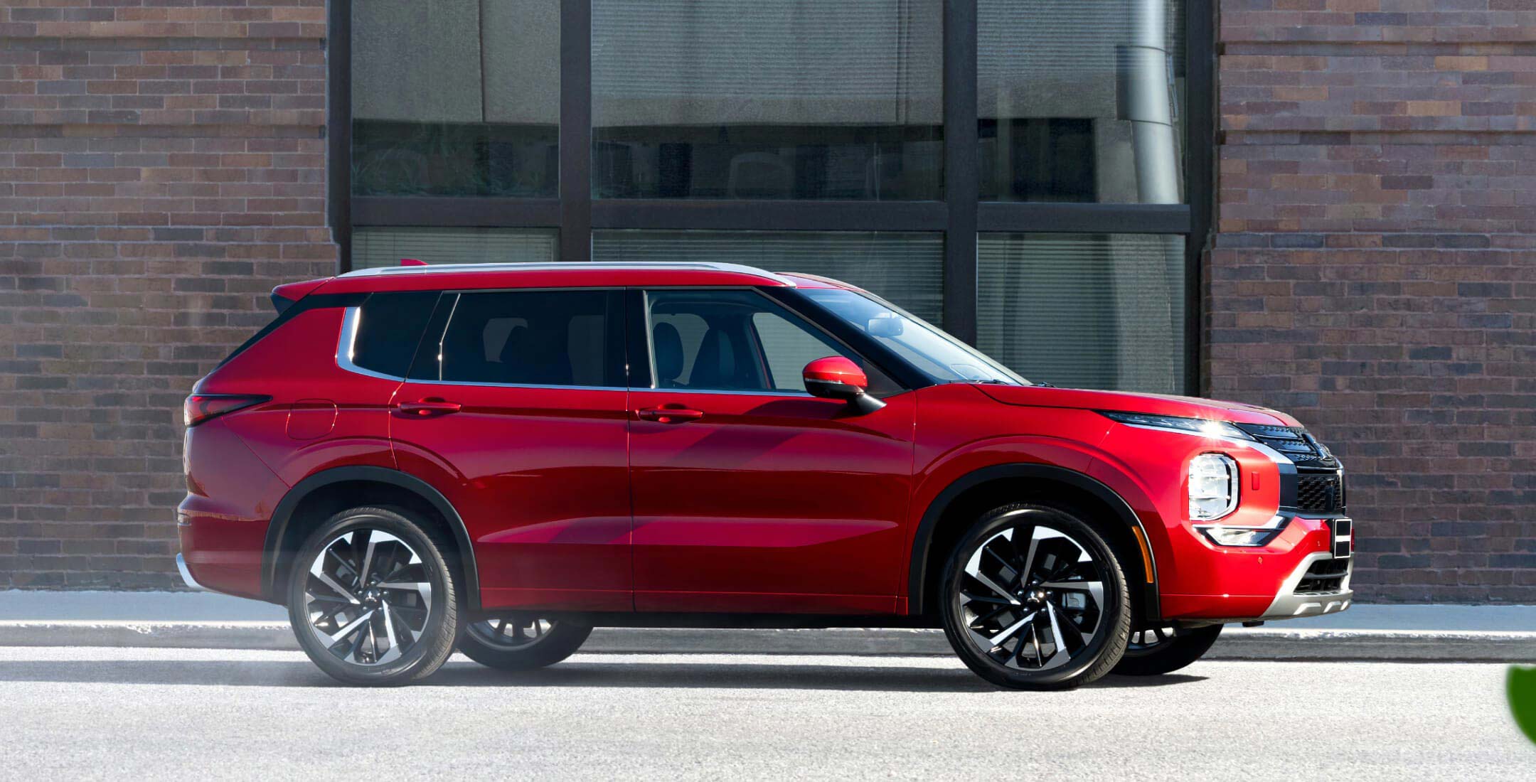 Side profile of a red diamond 2023 Mitsubishi Outlander SUV parked on the road.