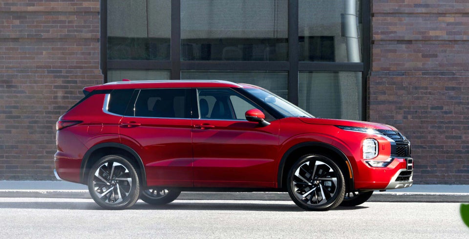 Side profile of a red diamond 2024 Mitsubishi Outlander SUV parked on the road.